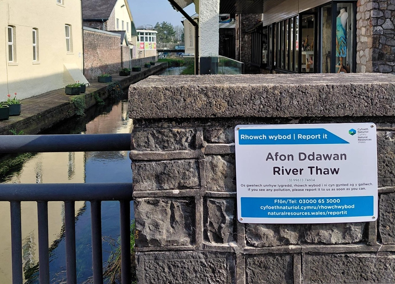 Arwydd wedi'i osod ar wal wrth ymyl afon