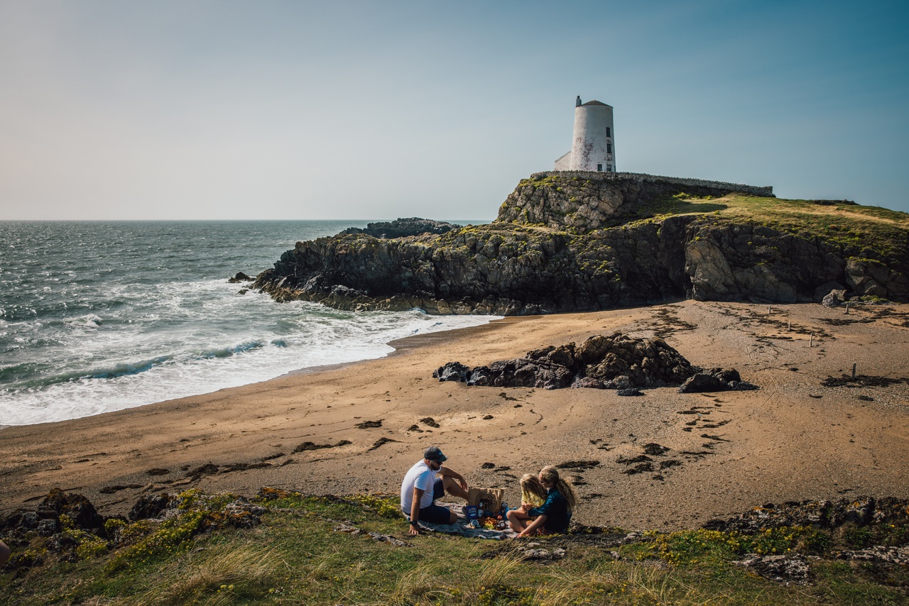 Pobl yn eistedd wrth Oleudy Ynys Llanddwyn